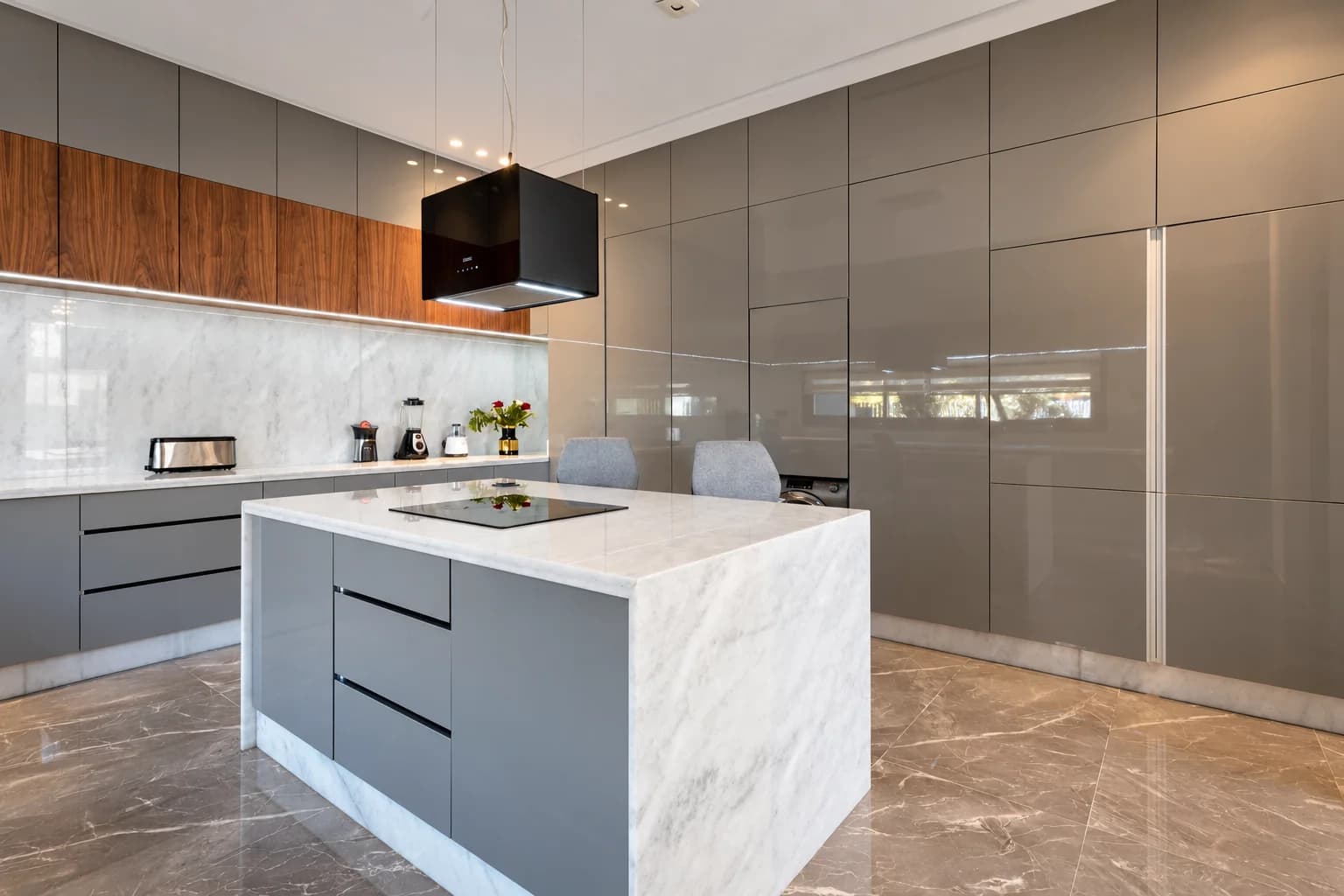 Cuisine de la Villa LEANA avec îlot central blanc, plaque de cuisson et rangements gris et bois.