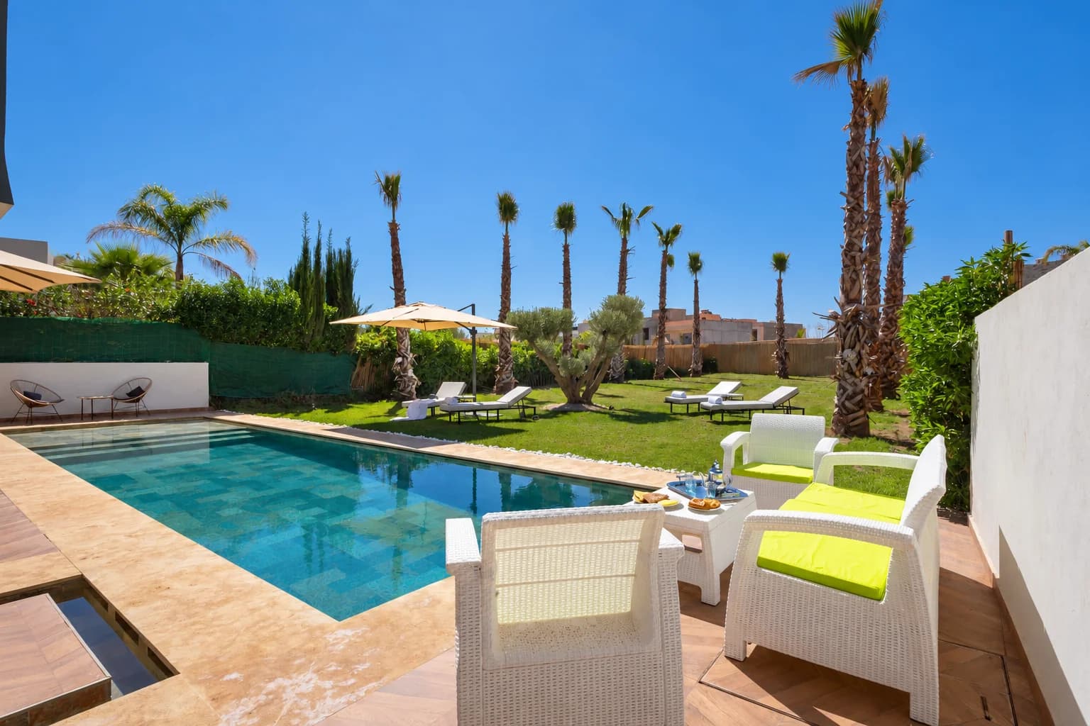 Piscine de la Villa LEANA bordée d’un salon de jardin blanc, de transats et de palmiers.