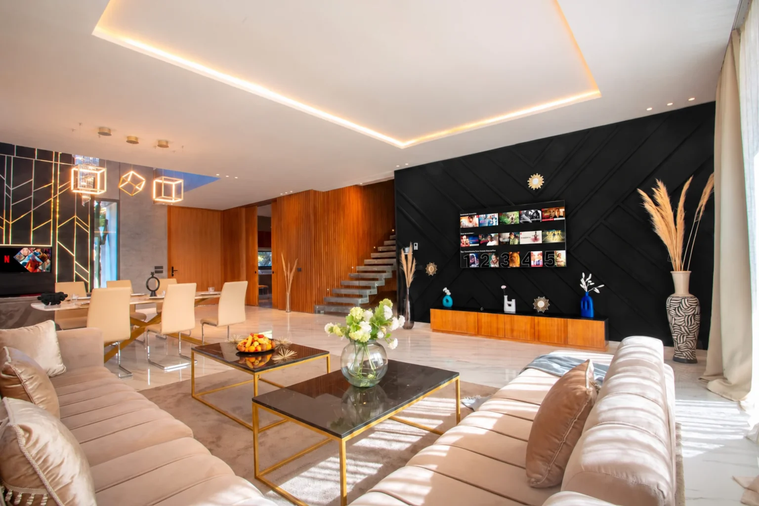 Salon de la Villa LEANA avec canapés beiges, tables basses, télévision et salle à manger.